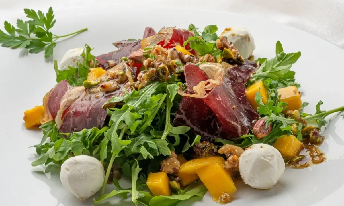 Deliciosa ensalada de cecina con mango, queso de cabra y nueces sobre rúcula fresca.
