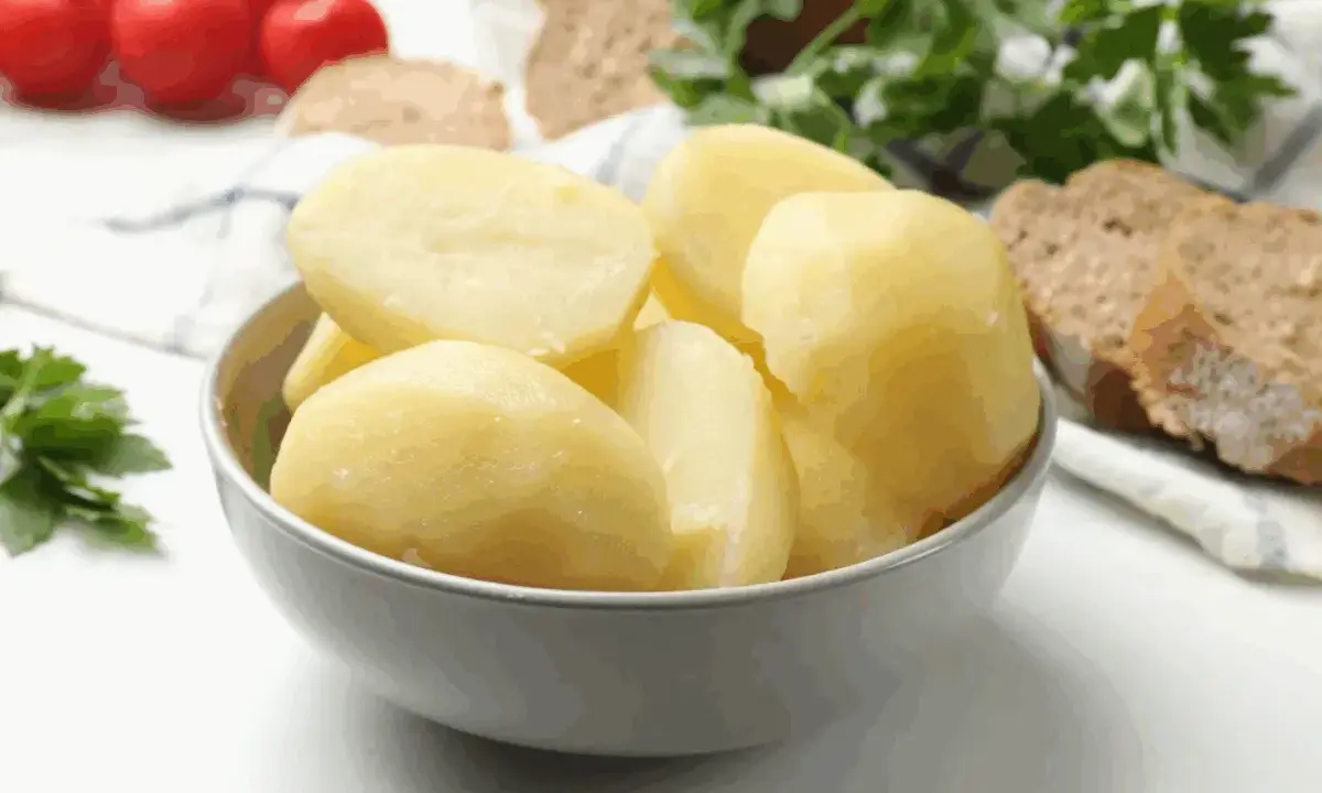 Un tazón lleno de patatas recién cocidas, listas para acompañar un pan rústico y tomates.