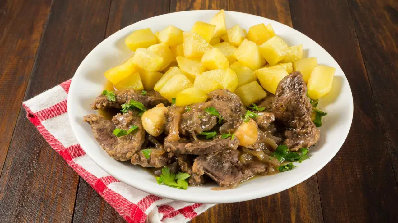 Plato de higaditos de pollo en salsa con patatas fritas en cubos, decorado con perejil fresco.