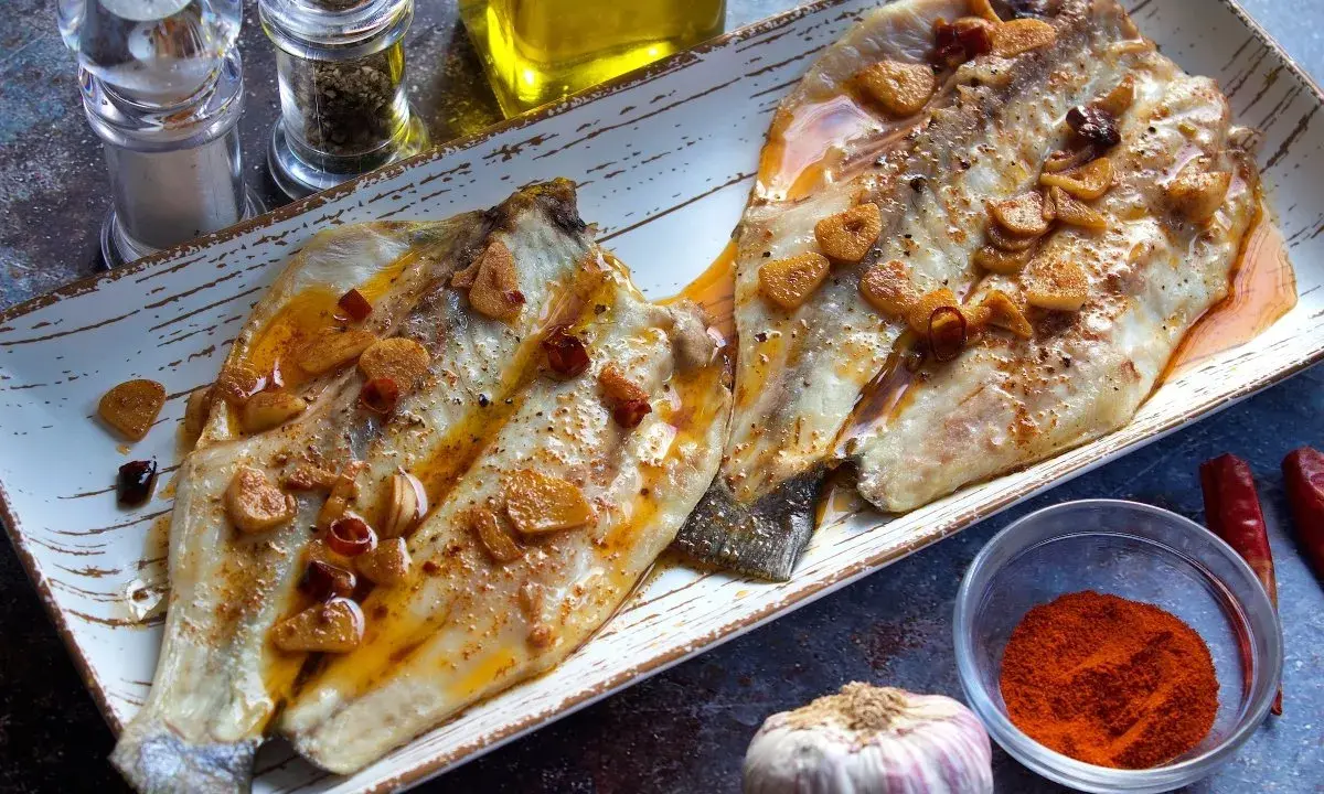 Dos filetes de lubina a la bilbaina, dorados y jugosos, con láminas de ajo y guindilla.