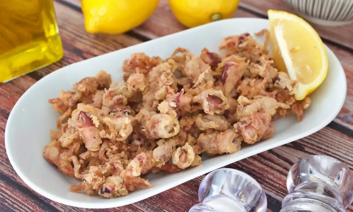 Crujientes puntillas de calamar fritas en un plato blanco, acompañadas de limón y aceite de oliva.