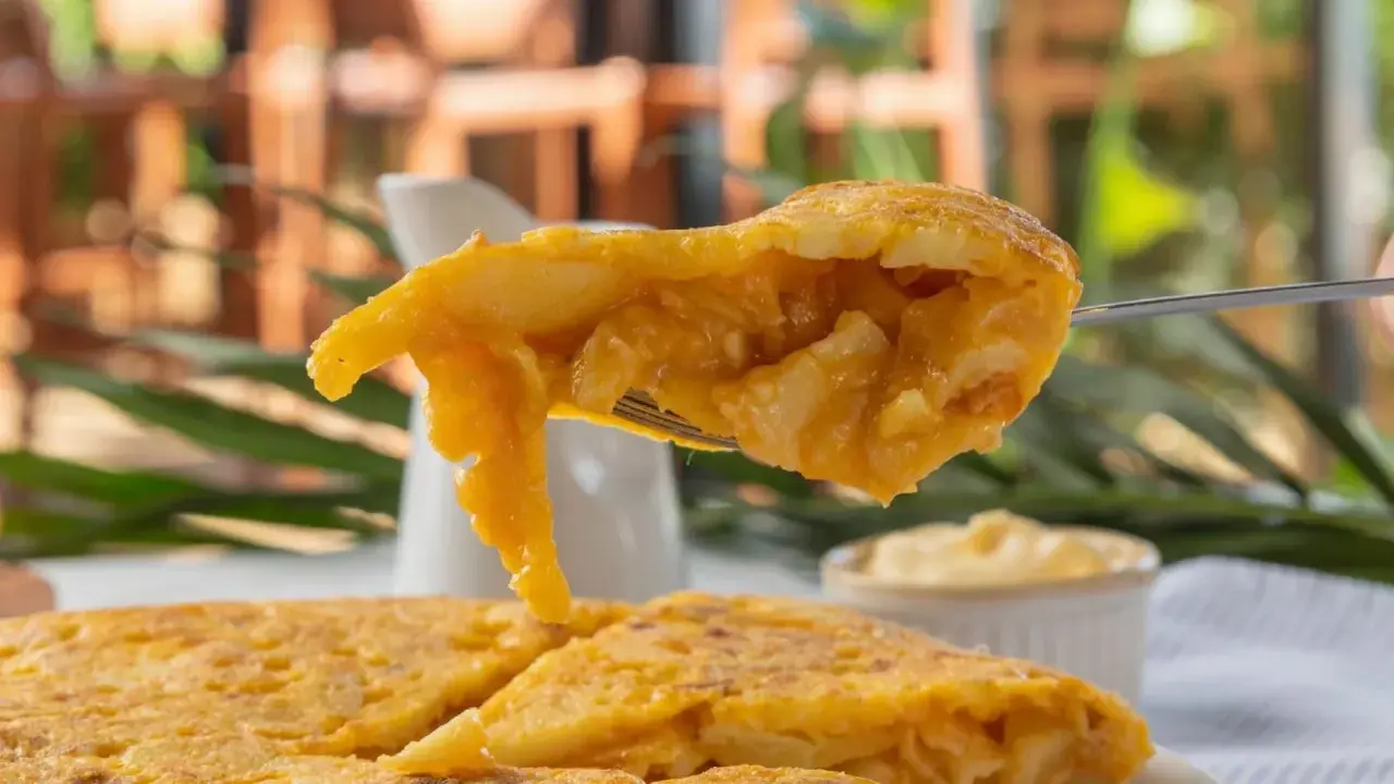 Un tenedor levanta un trozo de tortilla de patatas jugosa, mostrando su interior tierno y dorado.
