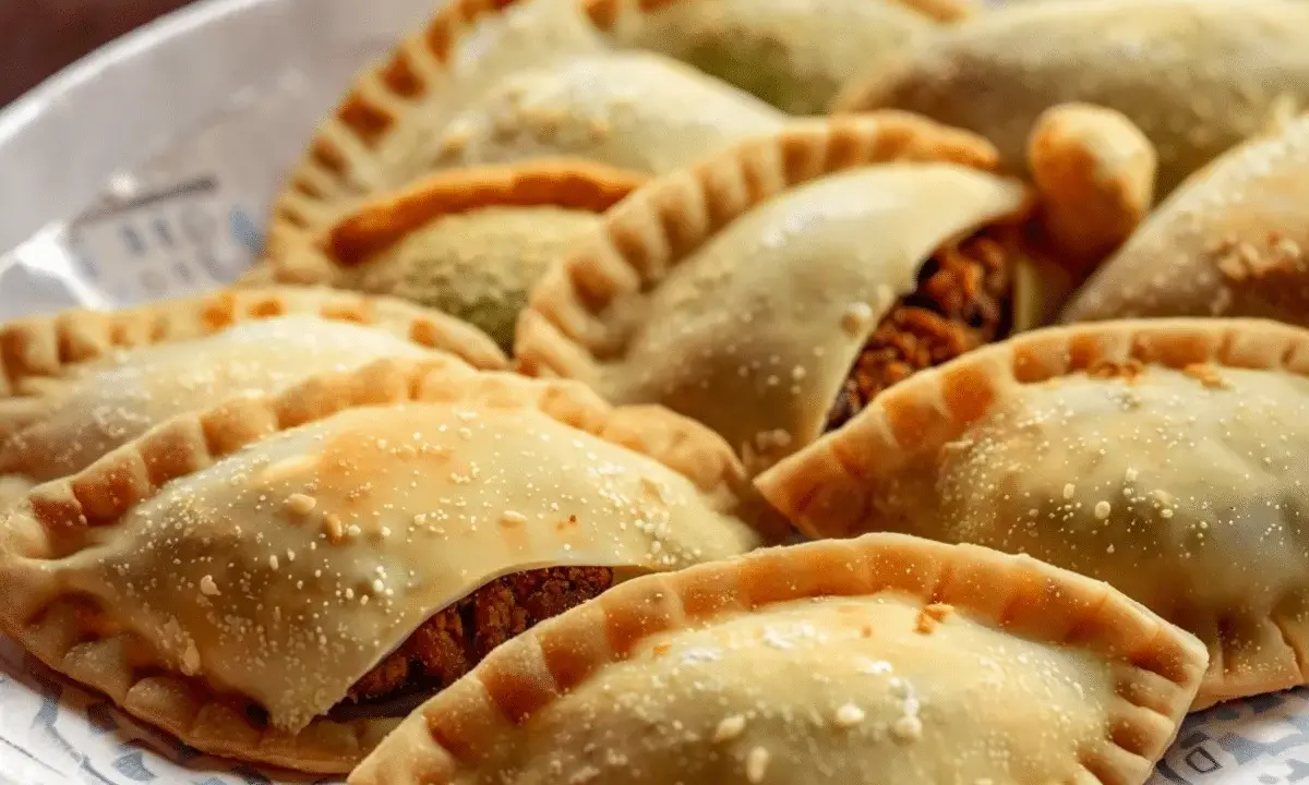 Empanadas doradas y crujientes, algunas con relleno visible de pechuga empanada, espolvoreadas con algo de sal.