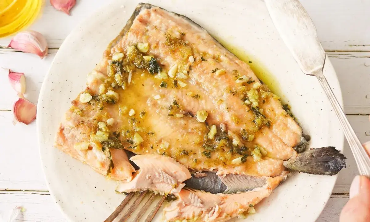 Deliciosa trucha al ajillo servida en un plato, con ajos y aceite de oliva alrededor.