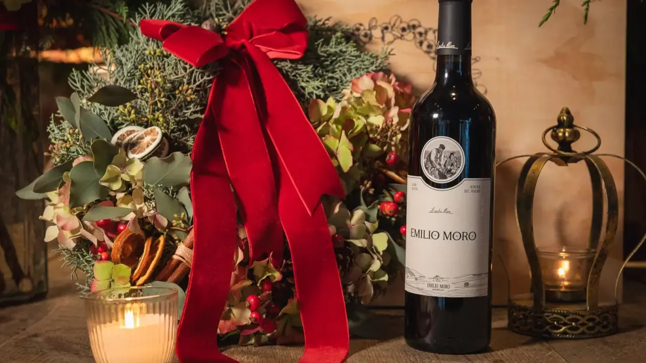 Botella de vino tinto fino Emilio Moro junto a un arreglo floral navideño, vela encendida y un candelabro dorado.