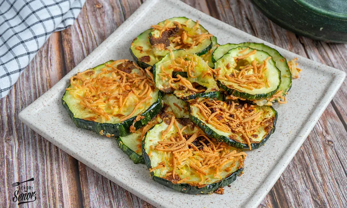 Rodajas de calabacín en freidora de aire, doradas y crujientes, con un toque de queso rallado. ¡Un snack saludable y delicioso!