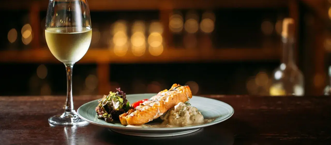 Un filete de salmón a la parrilla con ensalada y una copa de vino blanco, perfecto para un maridaje con riesling.