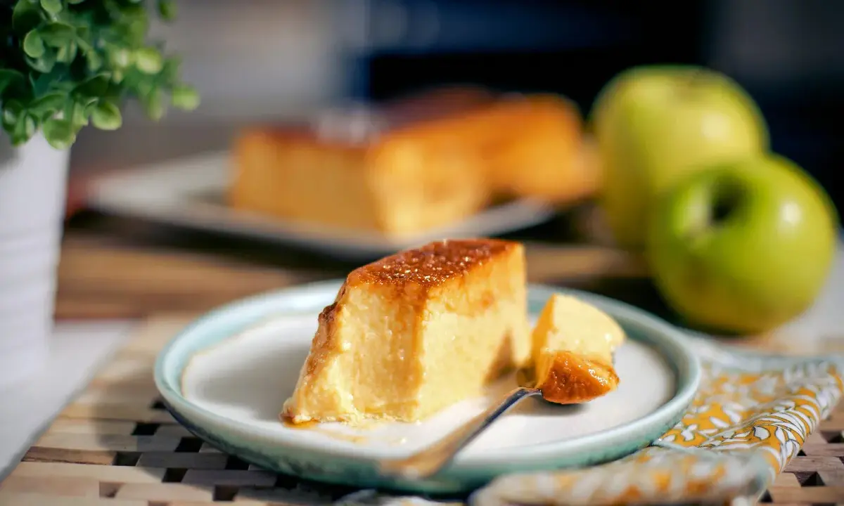 Un delicioso flan de manzana, con una porción servida en un plato, acompañado de manzanas verdes y una planta decorativa.