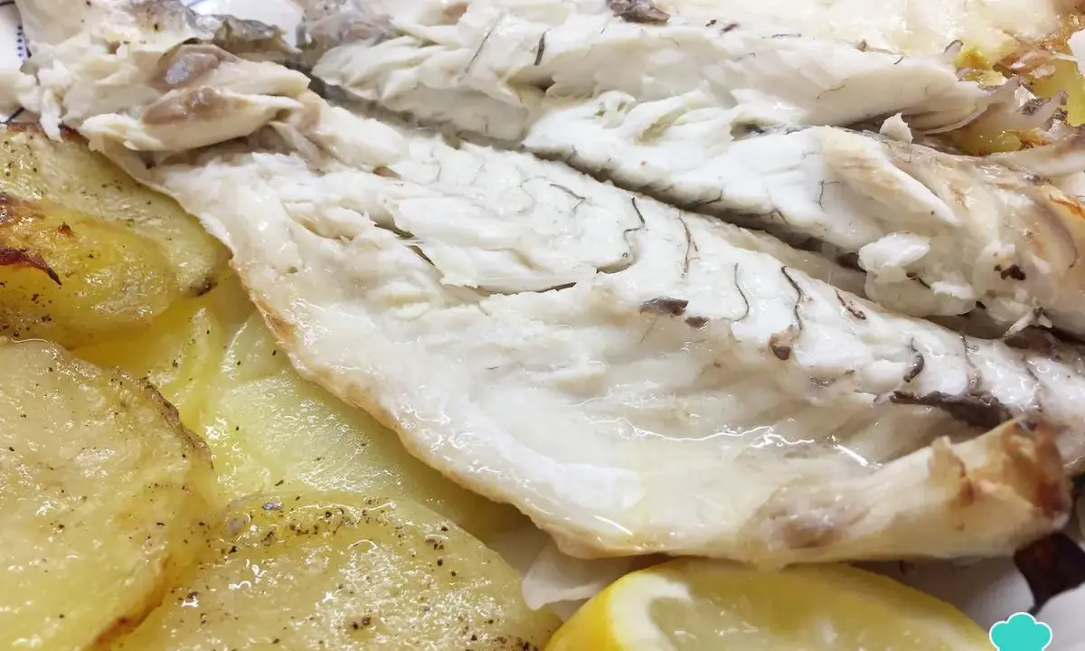Lubina al horno jugosa y tierna, acompañada de patatas doradas y una rodaja de limón. ¡Un plato delicioso y saludable!