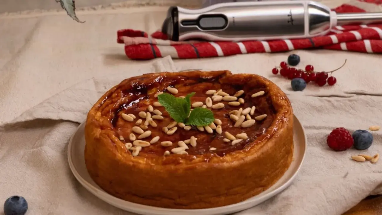 Bizcocho de avena casero, glaseado y decorado con piñones y menta. Frutos rojos y batidora al fondo.