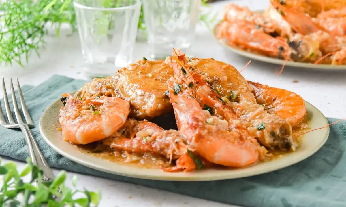 Plato de pollo con gambas en salsa, decorado con perejil picado. Se ve delicioso y listo para disfrutar.