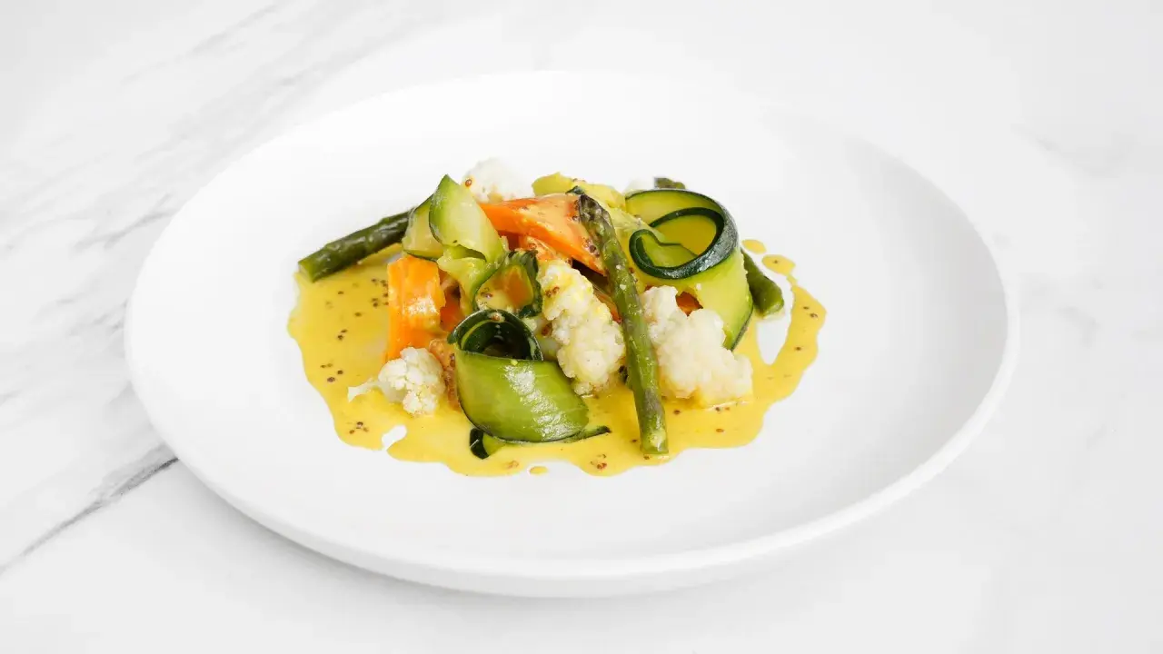 Deliciosas verduras al vapor, como zanahoria, calabacín en espiral, espárragos y coliflor, bañadas en una cremosa salsa amarilla.