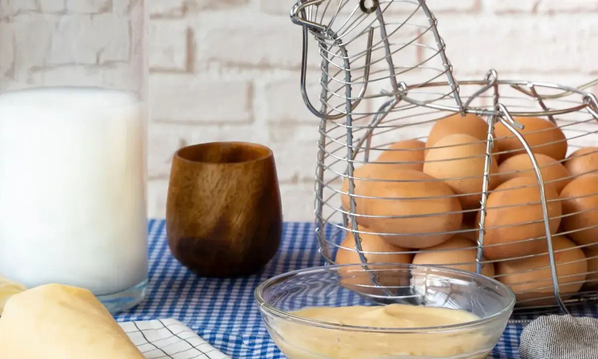 Crema pastelera lista para usar, hecha con Thermomix. Huevos frescos en cesta de gallina, leche y utensilios de repostería.