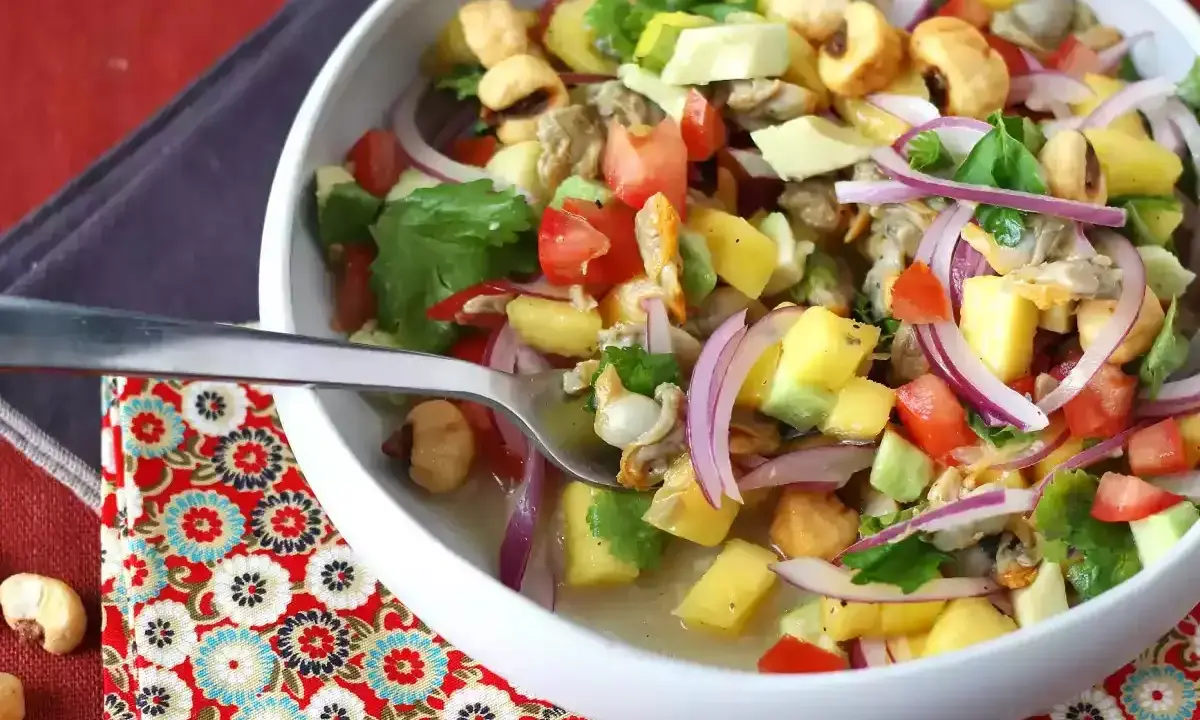 Un refrescante ceviche de berberechos con trozos de mango, aguacate, tomate y cebolla morada, servido en un cuenco blanco.
