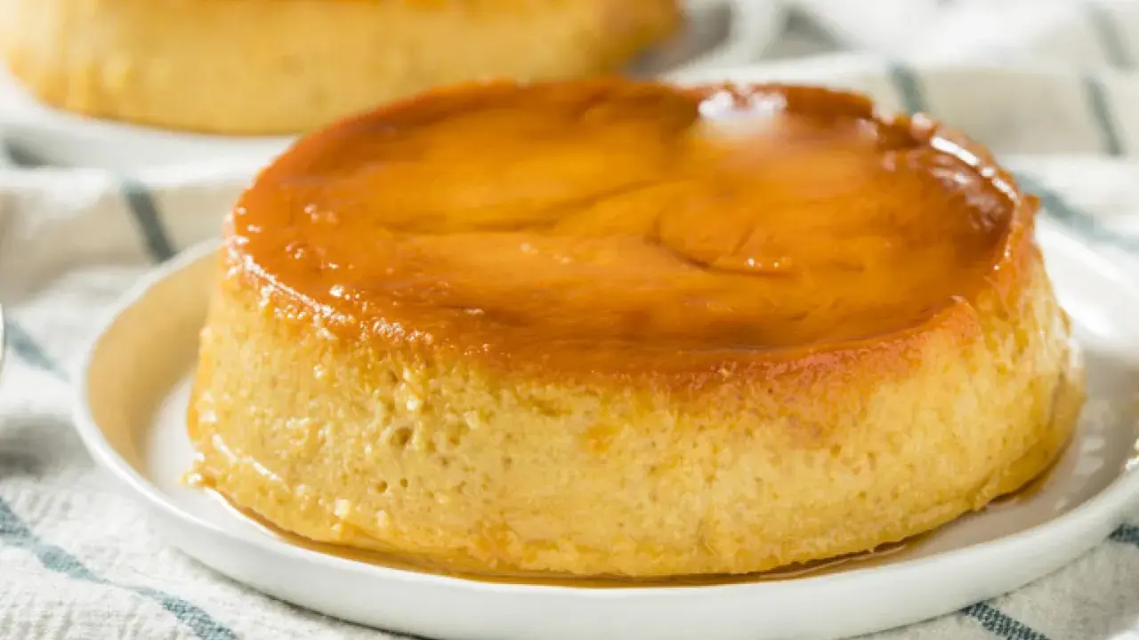 Delicioso flan de plátano con caramelo dorado, servido en un plato blanco sobre un mantel a rayas.