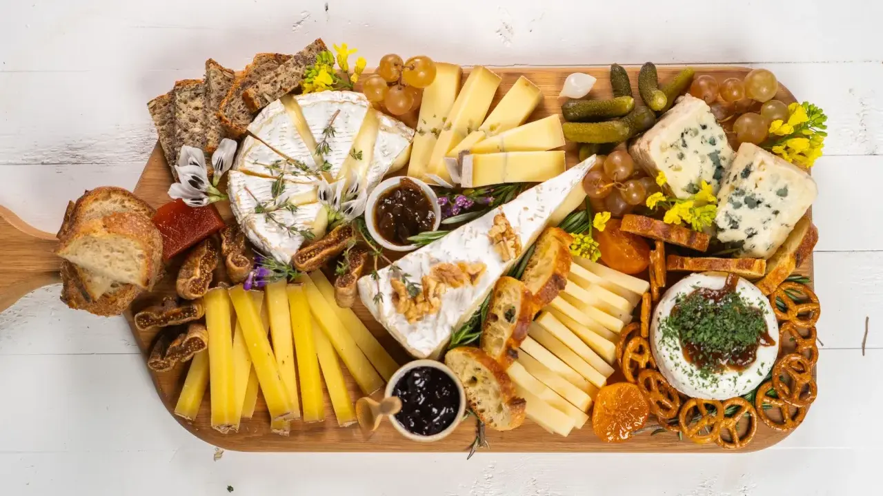 Una tabla de quesos sencilla con variedad de quesos, pan, frutas secas, uvas, pepinillos y mermelada.