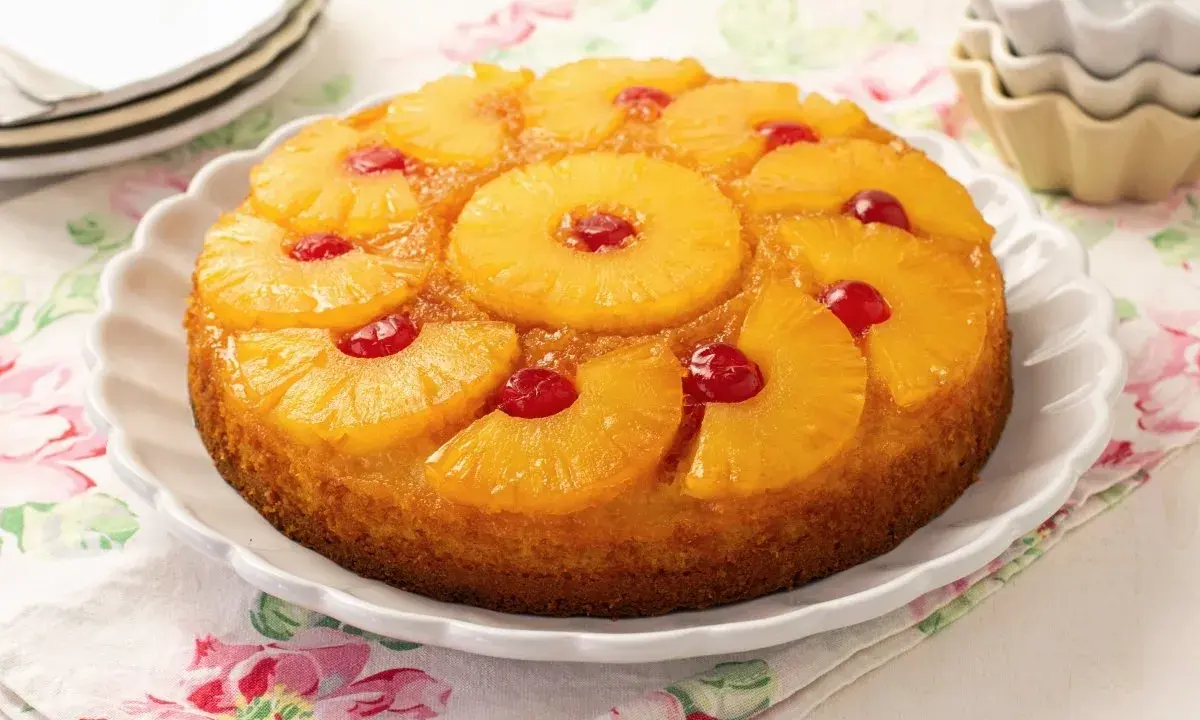 Tarta de piña dorada y jugosa, decorada con rodajas de piña caramelizada y cerezas rojas.