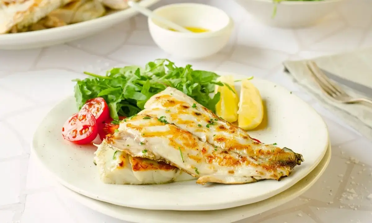 Deliciosa corvina a la plancha, servida con rúcula fresca, tomates cherry y gajos de limón. Un plato ligero y sabroso.