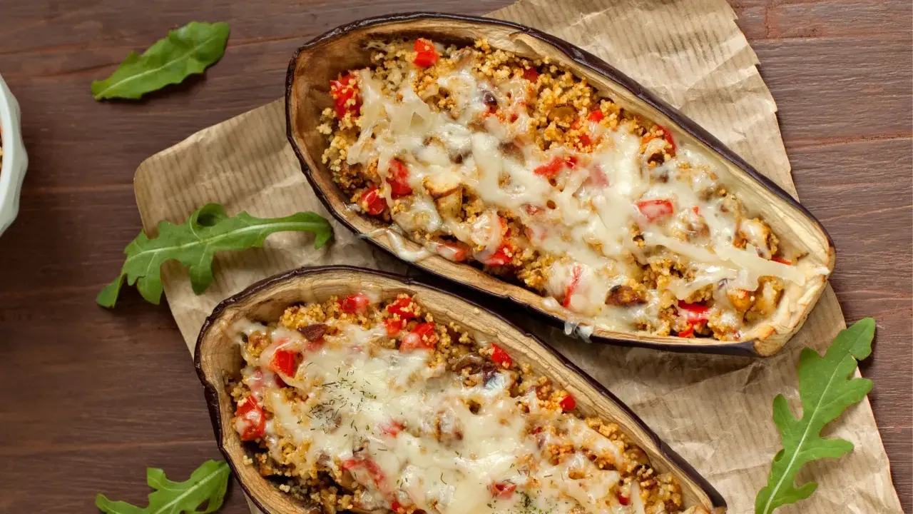 Dos mitades de berenjenas rellenas con cuscús, pimientos y queso derretido, cocinadas en airfryer.