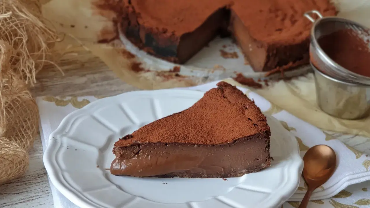 Un trozo de pastel de chocolate cubierto de cacao en polvo, con el pastel entero al fondo.