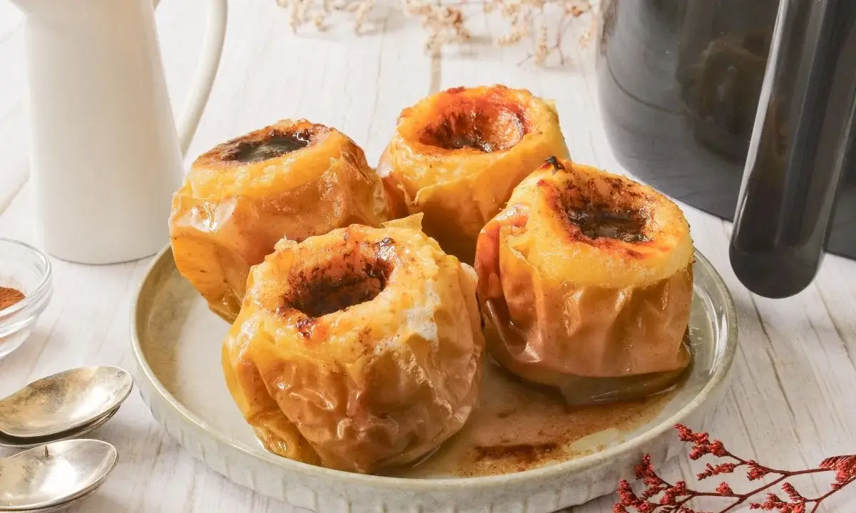 Cuatro manzanas asadas en freidora de aire, doradas y jugosas, con un relleno oscuro y especiado.