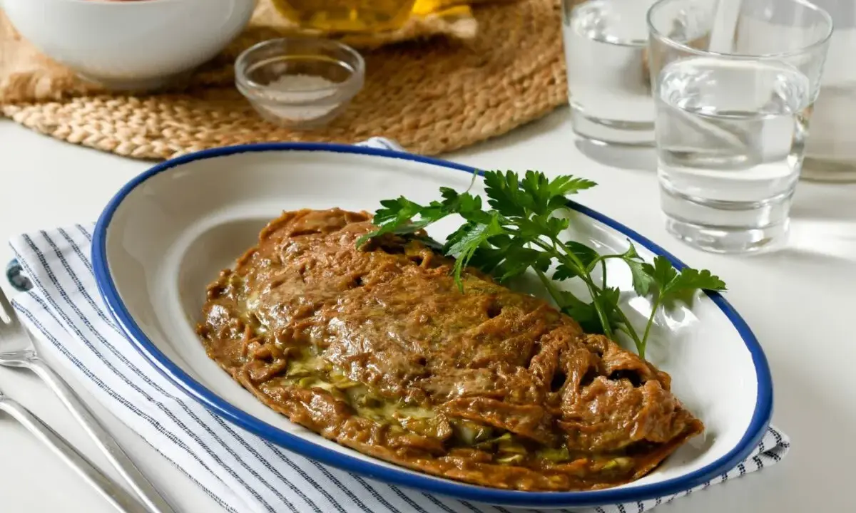 Tortilla de alcachofas dorada y jugosa, servida en plato blanco con borde azul. Decorada con perejil fresco.