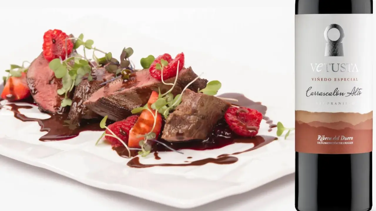 Filete de ternera con fresas y frambuesas, bañado en salsa, junto a una botella de vino Vetusta de la **Ribera del Duero**.