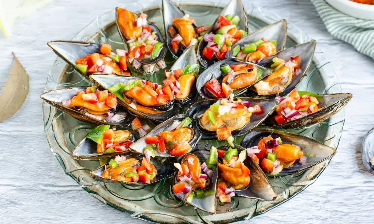 Mejillones a la vinagreta servidos en una bandeja de cristal, adornados con una colorida mezcla de pimientos y cebolla.
