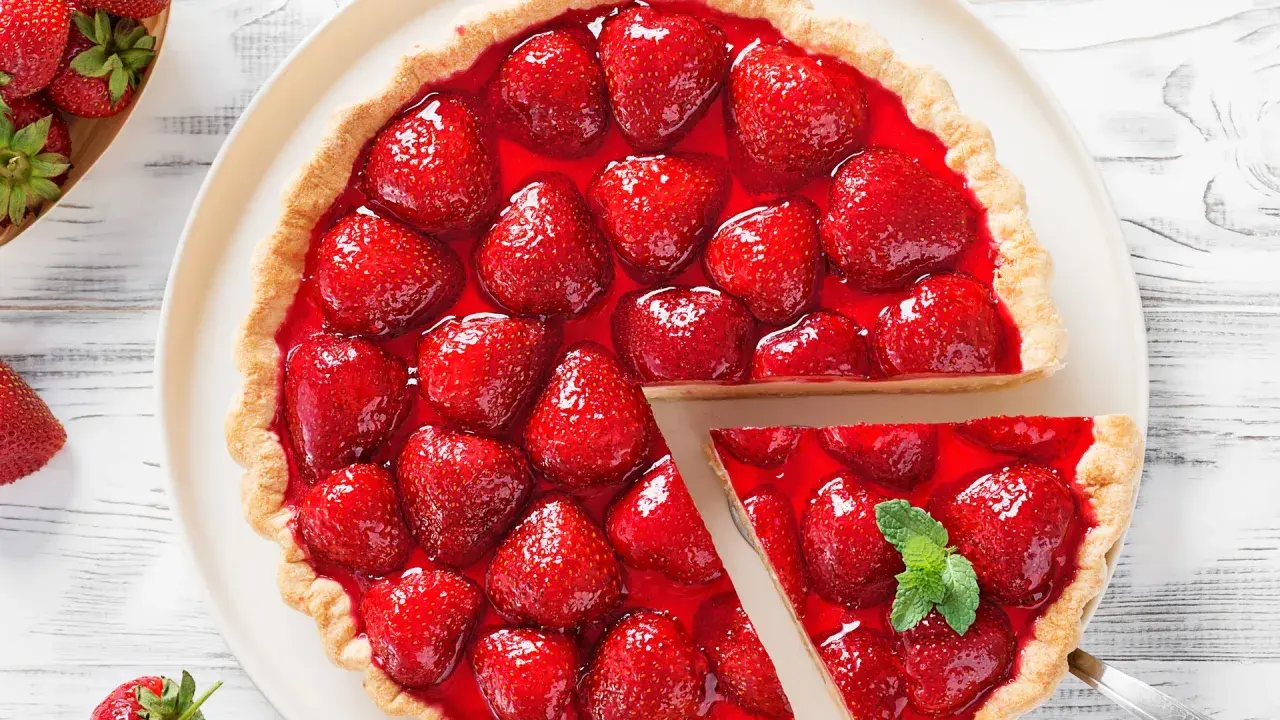 Deliciosa tarta de fresas cubierta con gelatina brillante y fresas frescas. Una porción se ha cortado, revelando la jugosa fruta.