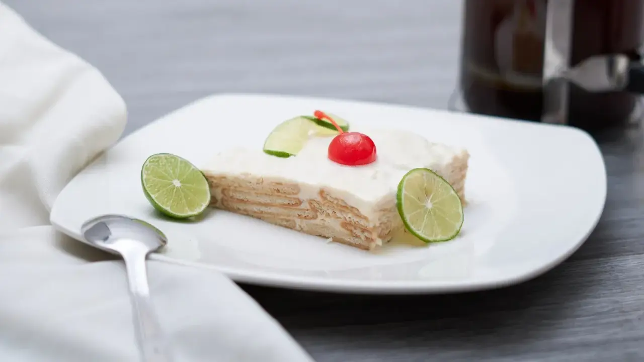 Deliciosa carlota de limón, con galletas y crema, decorada con rodajas de lima y una cereza.