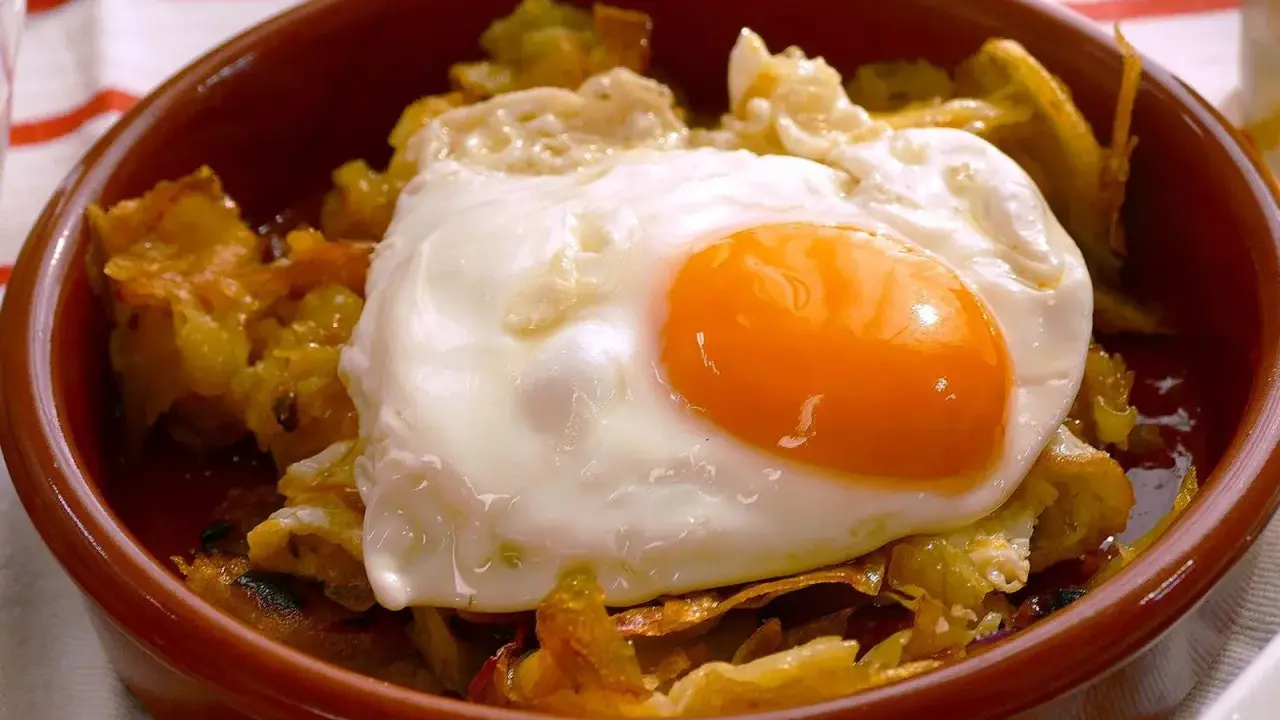 Un plato de patatas fritas con pimientos y un huevo estrellado encima, listo para disfrutar.