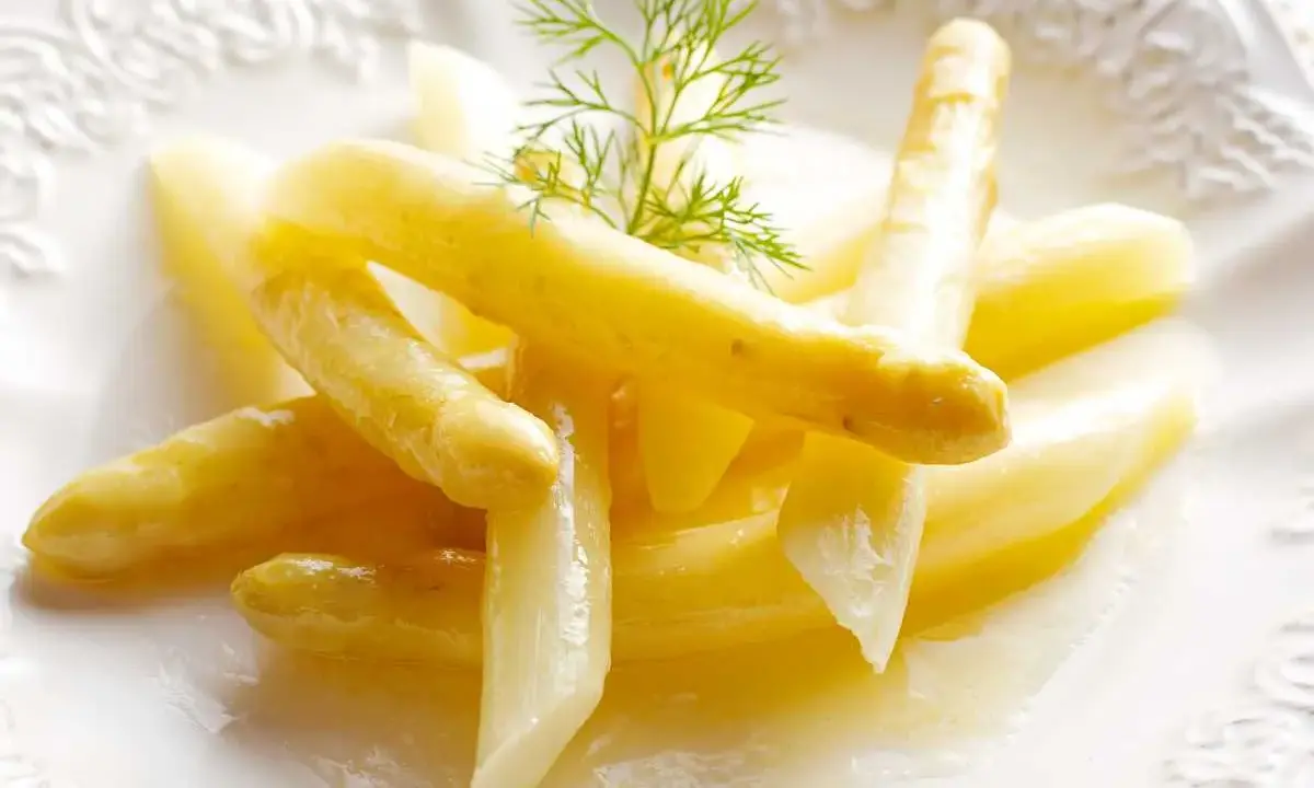 Espárragos blancos tiernos, listos para cocinar, servidos en un plato blanco con una ramita de eneldo.