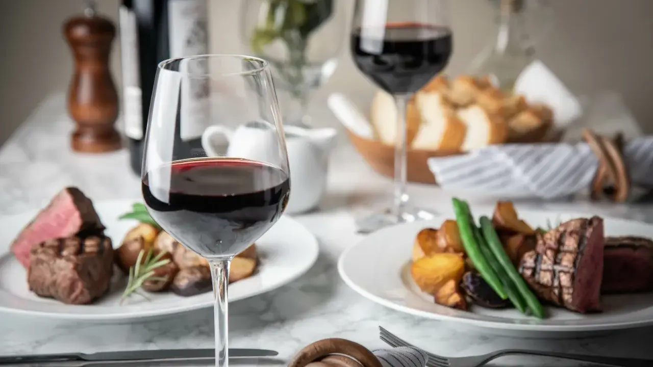 Dos copas de vino tinto, filetes jugosos y patatas asadas, perfectos para una cena de vino de invierno.
