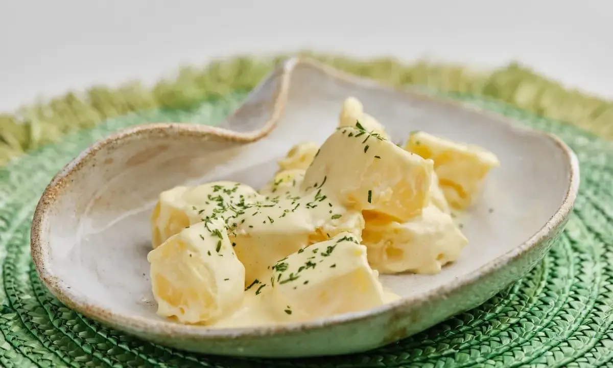 Patatas alioli cremosas y deliciosas, cubiertas con perejil fresco picado, servidas en un cuenco rústico sobre un salvamanteles verde.