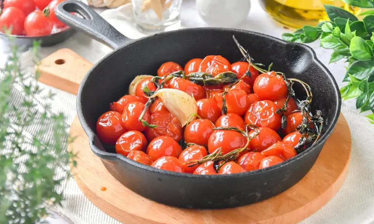 Tomates cherry confitados en sartén de hierro fundido, con ajo y hierbas aromáticas.