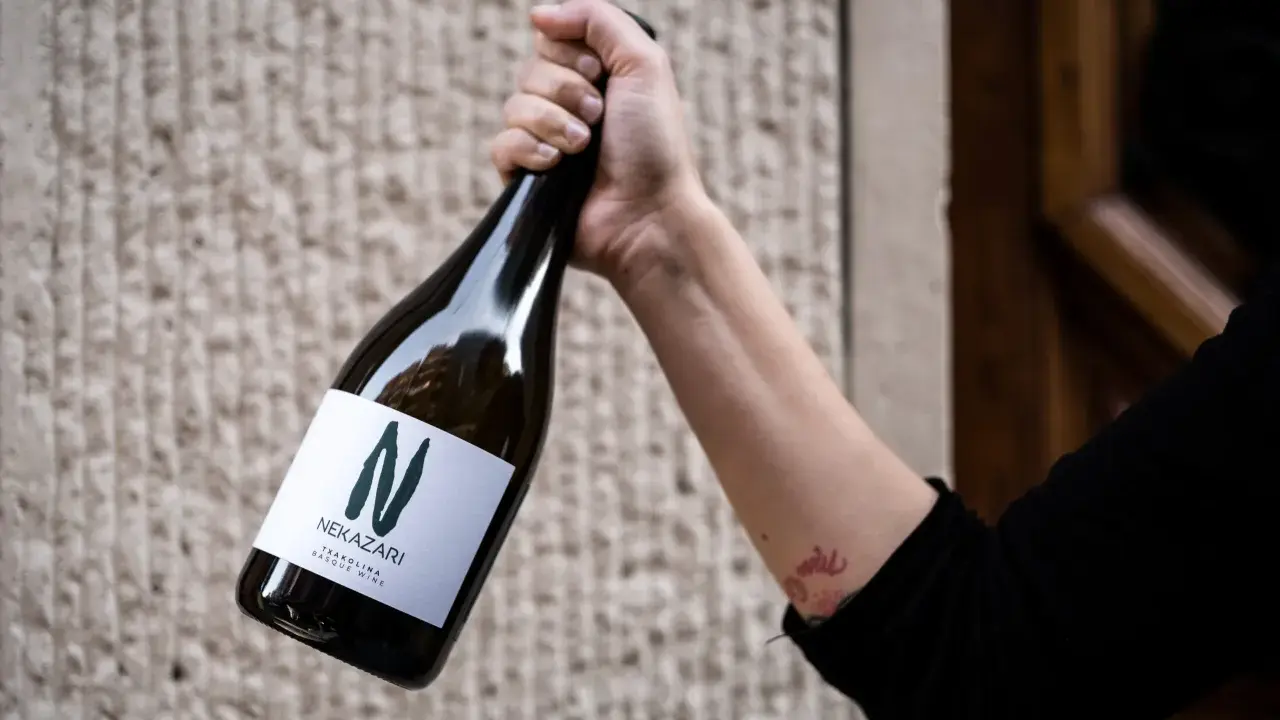 Mano sujeta botella de txakoli tinto Nekazari, con etiqueta blanca y letra "N" verde.