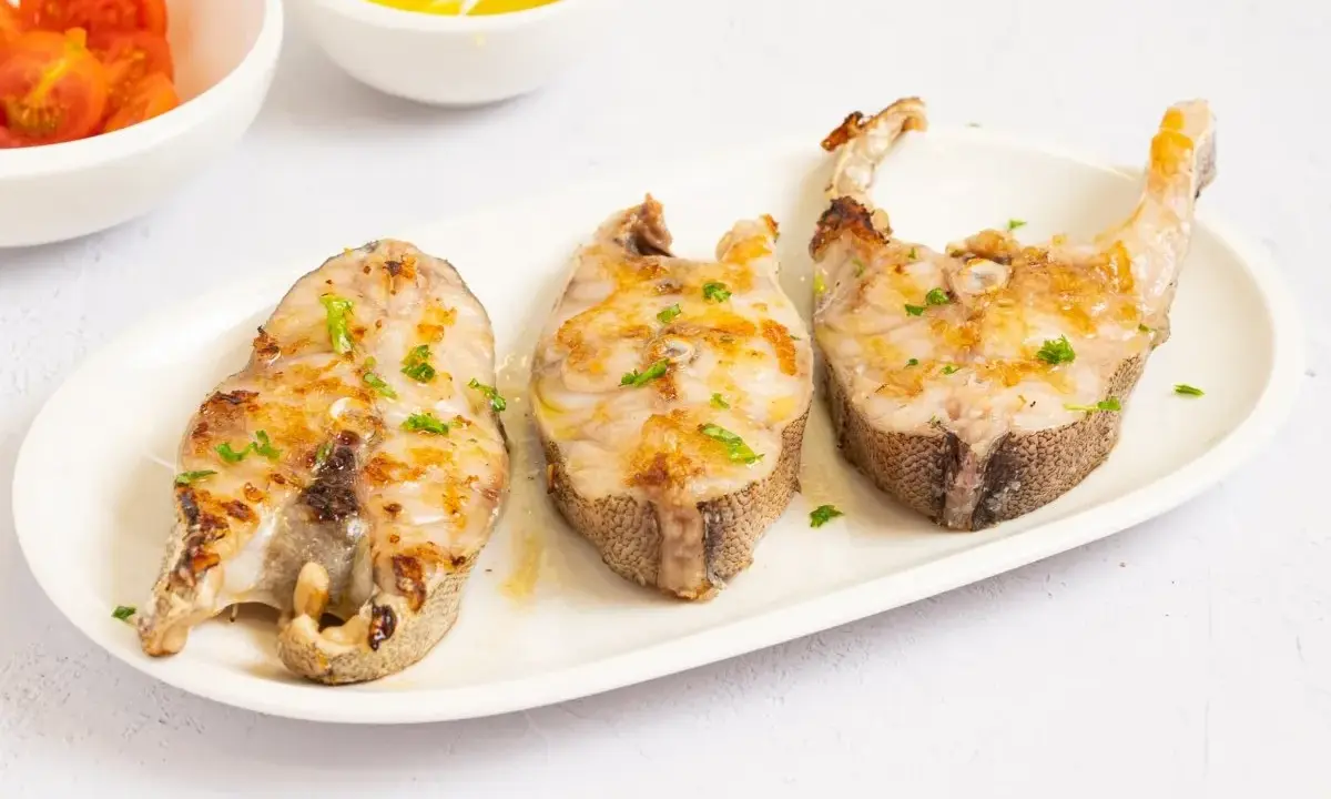 Tres rodajas de mero a la plancha, doradas y con perejil picado, servidas en plato blanco.
