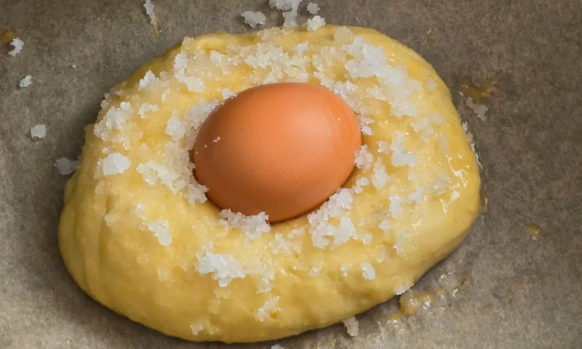 Masa para receta mona de pascua esponjosa, con un huevo crudo incrustado y espolvoreada con azúcar.