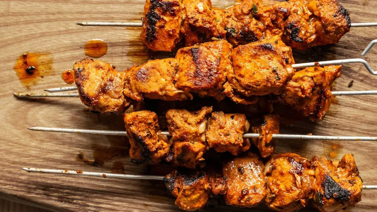 Cuatro brochetas de pinchos morunos auténticos, jugosos y dorados, sobre una tabla de madera.