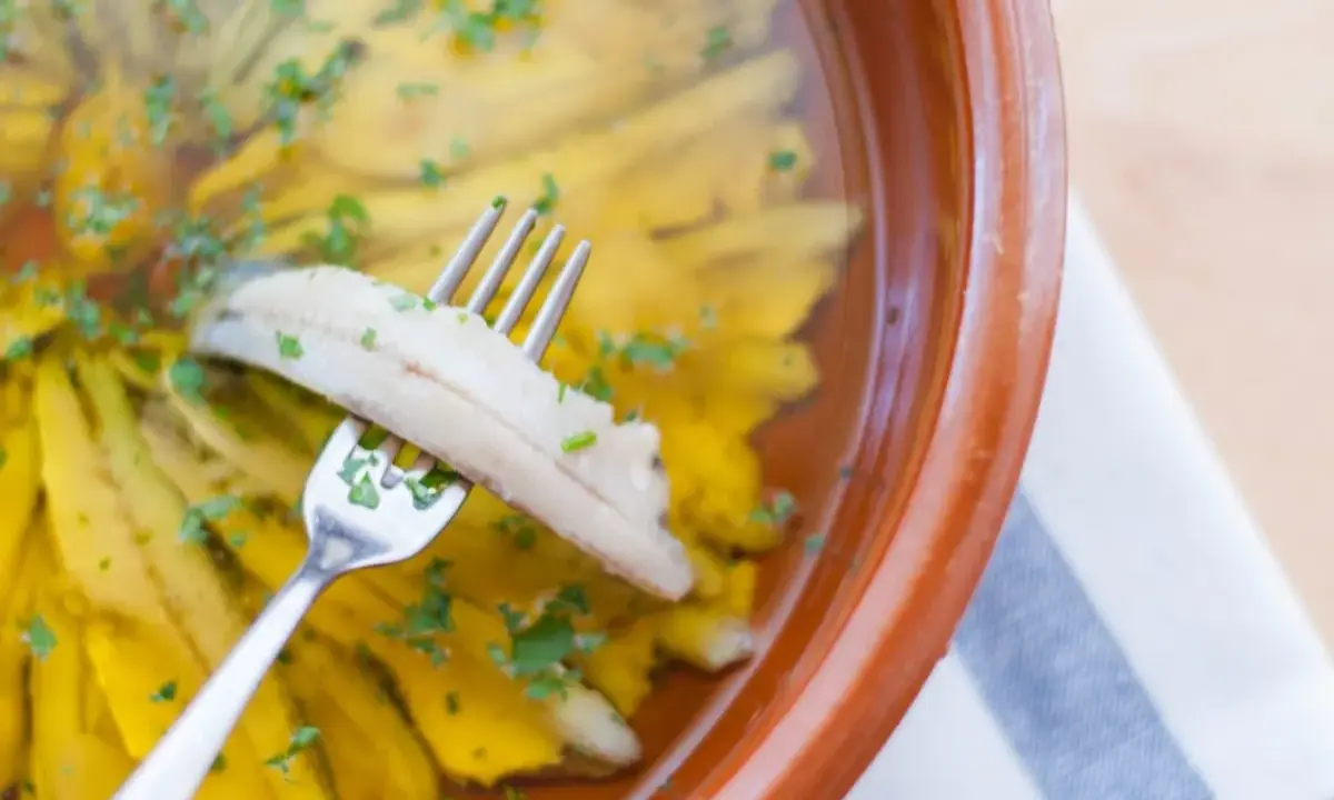 Boquerones en vinagre, la receta de la abuela, listos para disfrutar. Un tenedor recoge un boquerón marinado en aceite y vinagre, espolvoreado con perejil.