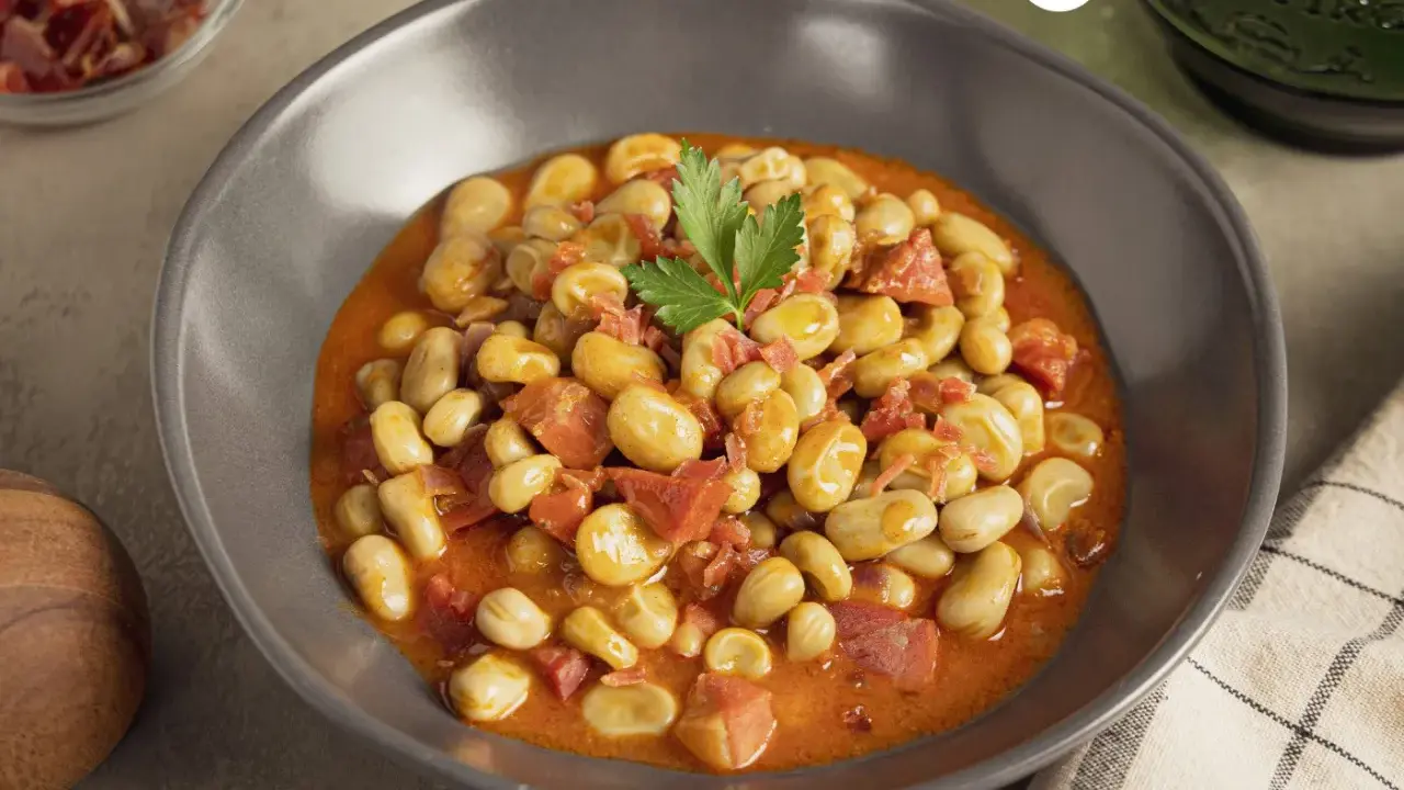 Plato de habas con jamón, guisadas en una salsa rojiza y decoradas con perejil.