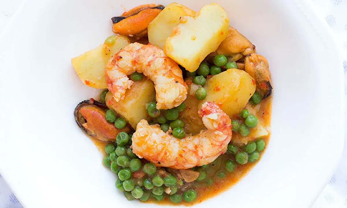 Patatas a la marinera con gambas, mejillones y guisantes en una salsa sabrosa.
