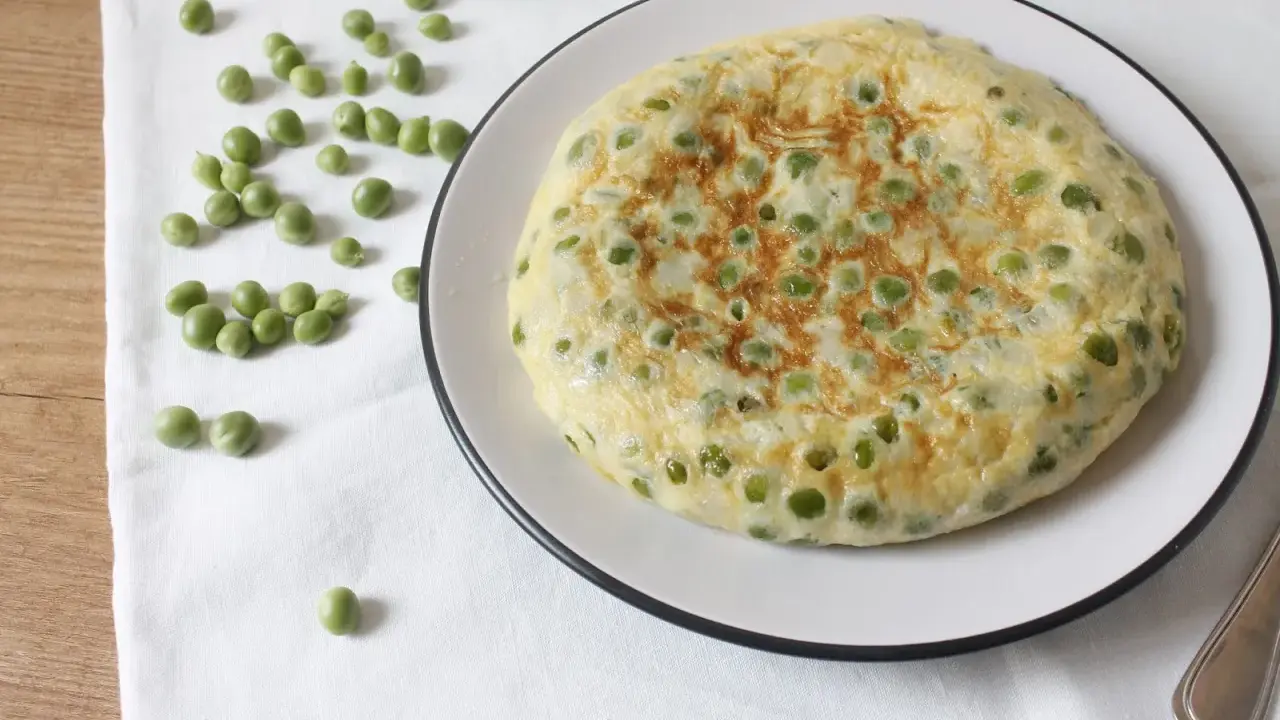 Tortilla de guisantes recién hecha, dorada y esponjosa, con guisantes verdes esparcidos por encima.