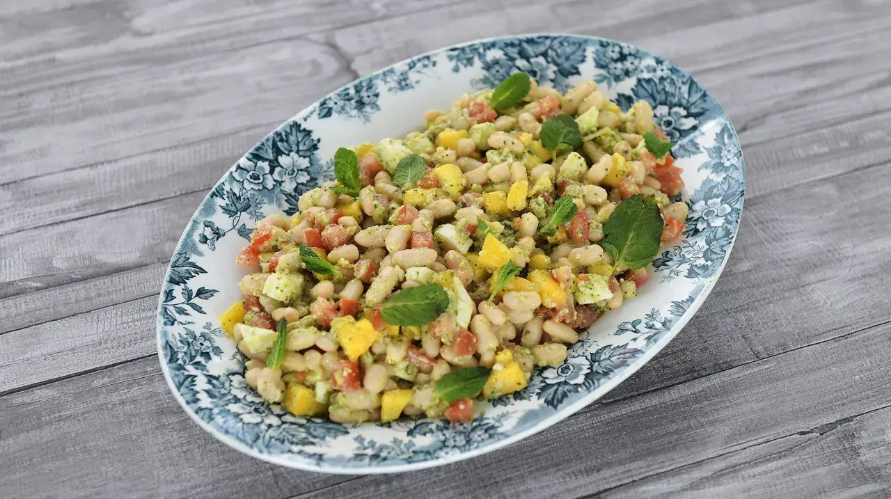 Deliciosa ensalada de alubias con trozos de tomate, mango y huevo, decorada con hojas de menta fresca.