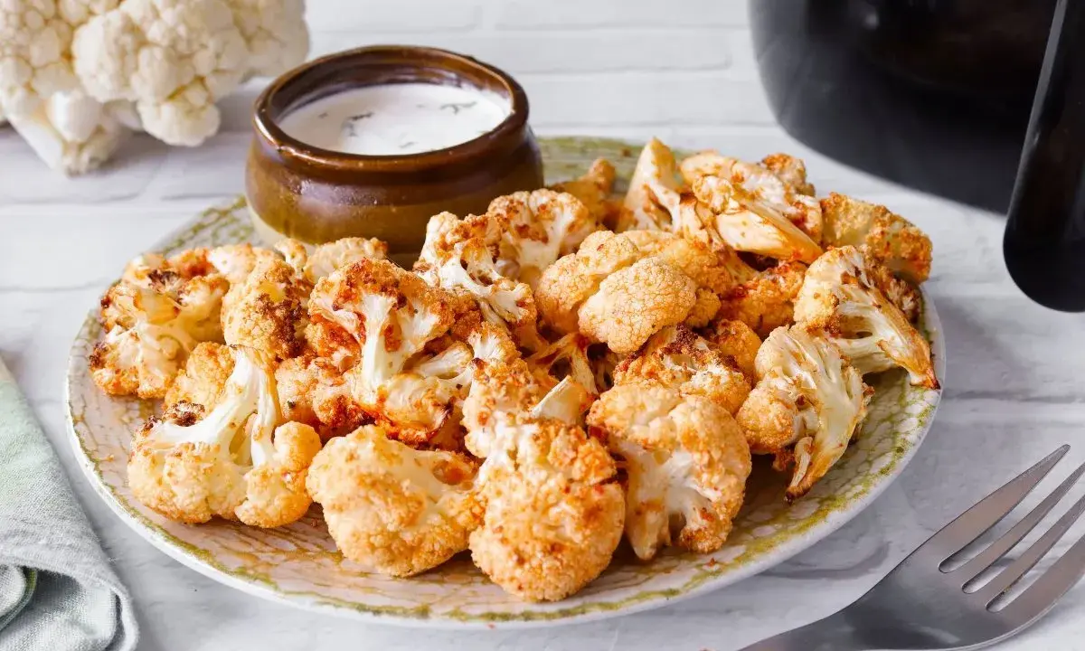 Coliflor airfryer dorada y crujiente servida en un plato con un tazón de salsa.