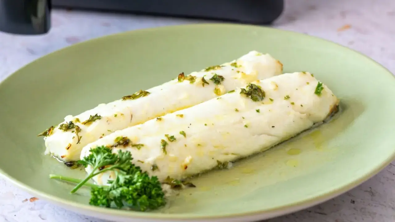 Dos filetes de merluza jugosos, recién salidos de la airfryer, con hierbas frescas y aceite de oliva.