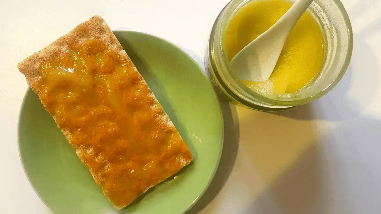 Galleta con mermelada de aceite de oliva, servida en plato verde junto a un tarro con la mermelada y una cuchara.