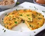Tortilla de atún dorada y esponjosa, espolvoreada con perejil fresco. Un trozo cortado revela la textura jugosa.