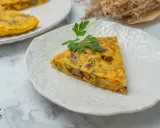 Un trozo de tortilla paisana, con patatas, verduras y chorizo, servida en un plato blanco texturizado.