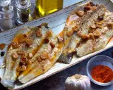 Dos filetes de lubina a la bilbaina, dorados y jugosos, con láminas de ajo y guindilla.